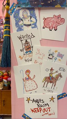 several children's drawings are hanging on a pink wall in front of other items