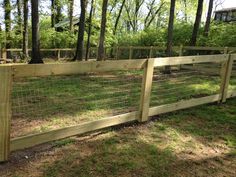 a wooden fence in the middle of a grassy area with trees and bushes behind it