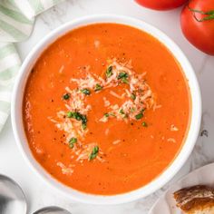 a bowl of tomato soup next to some bread and tomatoes