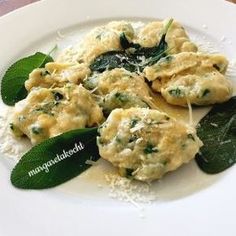 a white plate topped with ravioli covered in cheese and spinach leaf garnish