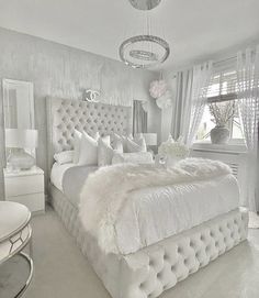 a white bedroom with an upholstered bed and chandelier