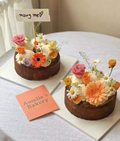 two cakes decorated with flowers on top of a table next to a sign that says annie's bakery