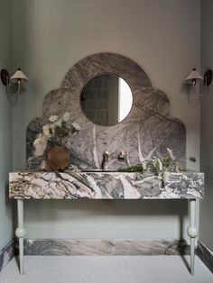 a bathroom with marble counter top and round mirror above the sink, along with two sconces