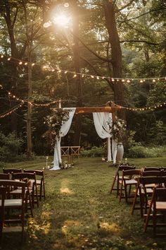 an outdoor wedding setup with white drapes and lights strung from the trees, surrounded by greenery