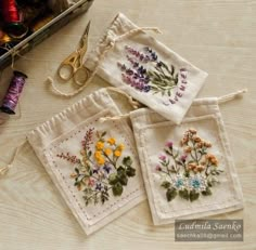 three small bags with flowers on them next to some scissors and thread spools