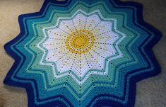 a crocheted blue and white blanket on the floor with a yellow sun in the center