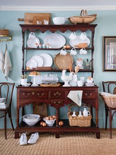 an old fashioned china cabinet with dishes and baskets on the top, sitting in front of a blue wall