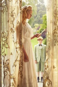 a woman standing in front of a window next to a little boy wearing a tuxedo