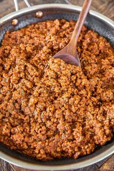 a skillet filled with ground beef and topped with a wooden spoon, on top of a wood table