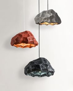 three different colored rocks hanging from strings against a white wall, one is orange and the other is black