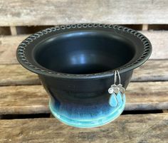 a black and blue bowl with silver earring hanging from it's side on a wooden bench