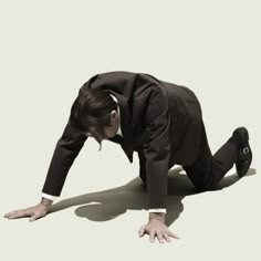 a man in a suit and tie bending over on the ground with his hands behind his head