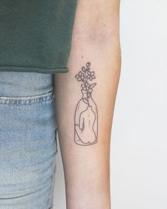 a person with a tattoo on their arm holding a flower in a bottle that is filled with water