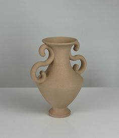 a white vase sitting on top of a table next to a gray wall and floor