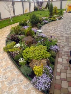 a garden with flowers and rocks in the middle on a brick walkway next to a fence