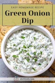 a white bowl filled with green onion dip surrounded by crackers