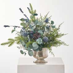 a vase filled with lots of green and blue flowers on top of a white table