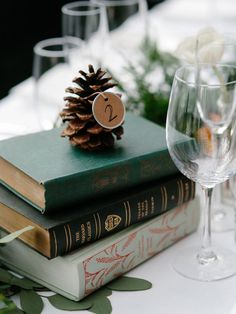 a stack of books sitting on top of a table next to wine glasses and a pine cone