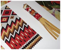 a cross stitch bookmark with two tassels on top of it, and an image of a flower in the background