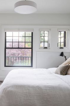 a white bed sitting under two windows in a bedroom