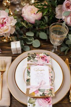 a place setting with pink flowers and greenery