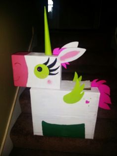 a cardboard box with a pink and green unicorn on it's head sitting on the stairs