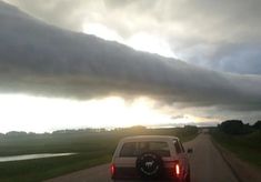 a car driving down a road with a large cloud in the sky