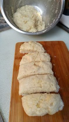 sliced bread sitting on top of a wooden cutting board next to a metal bowl and pan