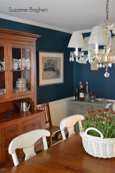 a dining room table with chairs and a basket on it's centerpiece, in front of a blue wall