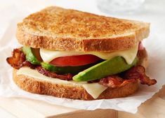 a sandwich with bacon, lettuce and tomato on it sitting on wax paper