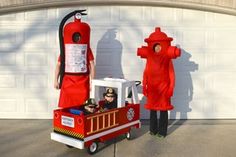 two people dressed as firemen are standing in front of a fire hydrant that is attached to a cart