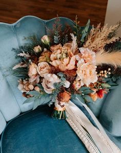 a bridal bouquet sitting on top of a blue velvet chair with feathers and flowers