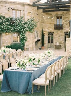 a long table set up with blue linens and white flowers in front of an old stone building