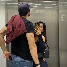 a man and woman standing next to each other looking at their cell phones in an elevator