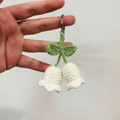 a hand holding a keychain with two white crocheted bells attached to it