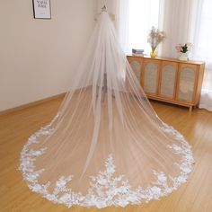 a wedding veil is hanging on the floor in front of a dresser and window with curtains