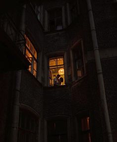 two people are standing in the window of an old building at night with their lights on