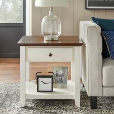 a white end table with a clock on it and a lamp in front of it