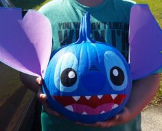 a young boy holding a blue pumpkin decorated with an elephant's head and teeth