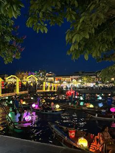 many small boats floating on top of a river at night with lights in the water