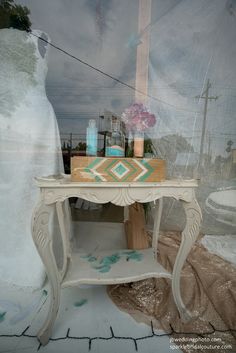 a white table sitting in front of a window next to a vase with flowers on it