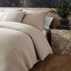 a bed with beige linens and pillows in a room next to a plant on a table