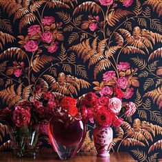 two vases filled with red and pink flowers on a table next to a wallpaper