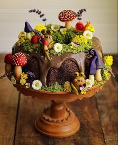 a cake that is sitting on top of a wooden table with mushrooms and flowers around it