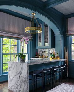 a kitchen with blue walls and marble counter tops, along with bar stools in front of the window