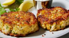 two crab cakes on a plate with lemon wedges