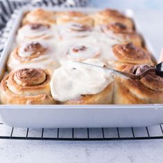 someone is spreading icing on top of some cinnamon rolls in a white baking dish