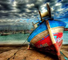 an old boat sitting on top of a beach next to the ocean under a cloudy sky