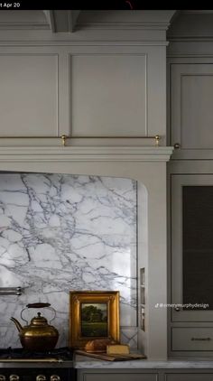 a kitchen with white marble counter tops and gold accents on the hood, cabinets and stove