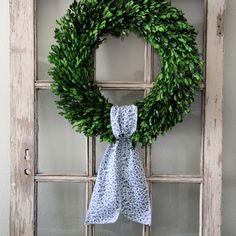 a wreath hanging on the front door with a blue and white scarf tied to it